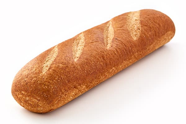 A freshly baked, golden-brown loaf of bread with three diagonal slashes on the top crust, resting on a white surface. The bread has a slightly rough texture and a cylindrical shape, indicating it might be a baguette or similar type of bread.