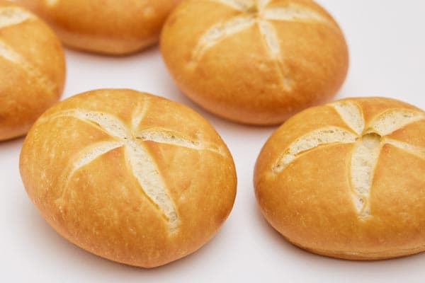 Five round, golden-brown bread rolls with star-shaped slashes on top are arranged on a plain white background.