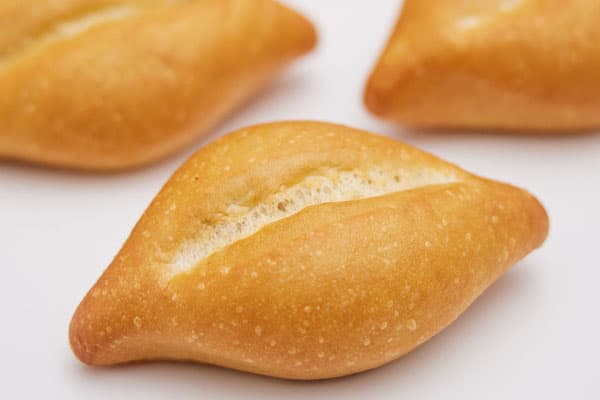 A close-up image of three freshly baked bolillo rolls on a white background. The golden-brown rolls have a slightly oval shape with a crisp outer crust and a prominent slit across the top, showcasing their soft, fluffy interior.