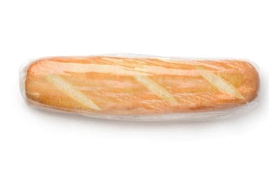 A loaf of French bread is wrapped in a clear plastic wrapper. The bread has a golden-brown crust with diagonal scoring marks on the top. The background is plain white.