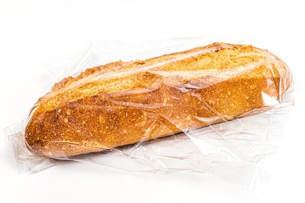 A loaf of crusty bread partially wrapped in clear plastic is displayed against a white background.