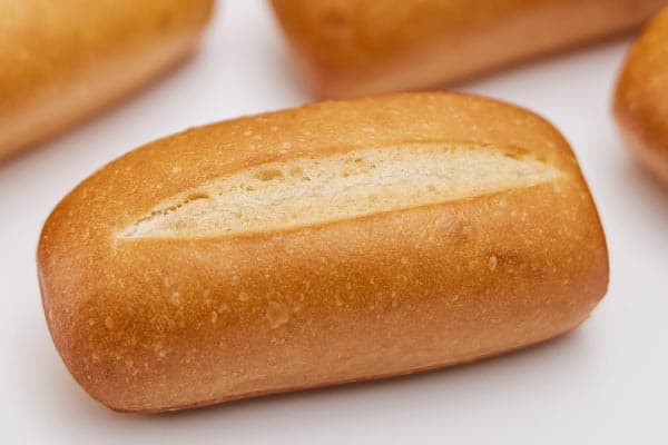 Four freshly baked baguettes with golden-brown crusts are placed on a perforated baking tray. Each baguette has several diagonal slashes on top, allowing steam to escape during baking, creating their signature texture.